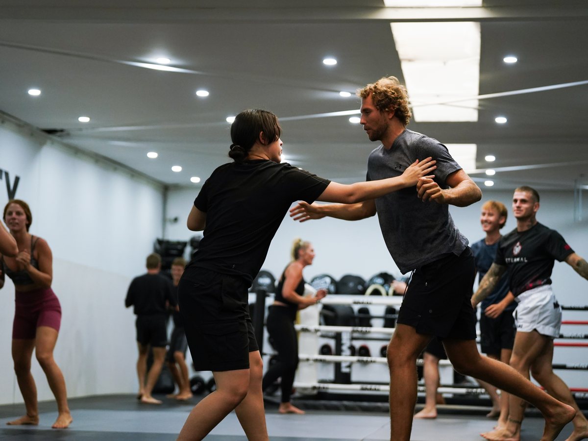 Two members working a partner drill in a Muay Thai class while others train and laugh behind them
