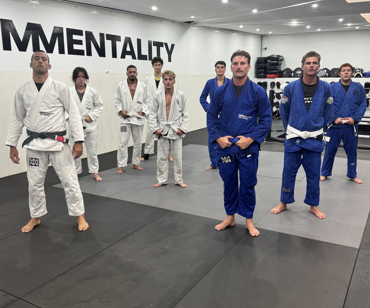 A Gi class of white belts through to black belt standing on the mats