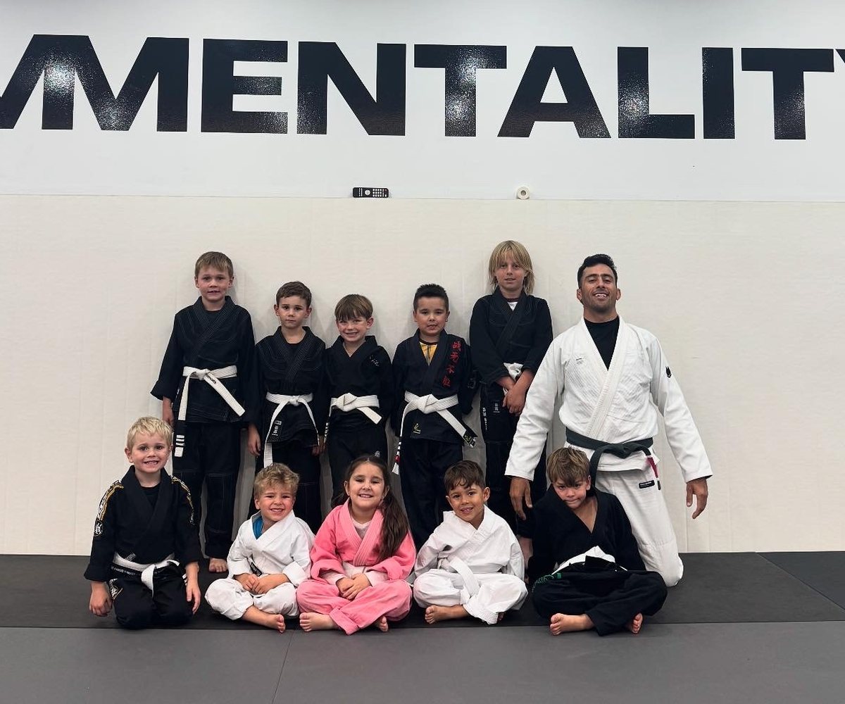 A Kids Jiu Jitsu class with their coach in front of the Mentality wall